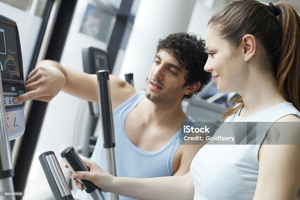 Trainer aiutando la donna su esercizio macchina passo-passo. - Foto stock royalty-free di Abbigliamento sportivo