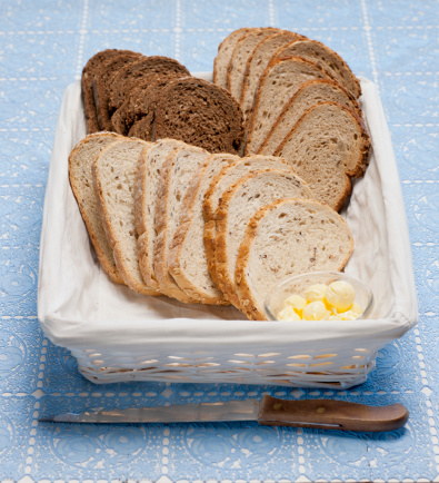 slices of brown and whole wheat bread in basket with butter balls in bowl