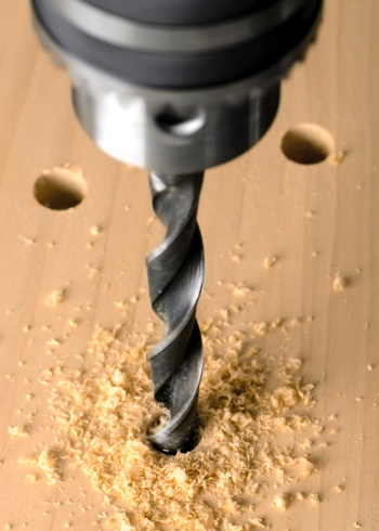 A close-up of a drill and twist bit drill into wood.