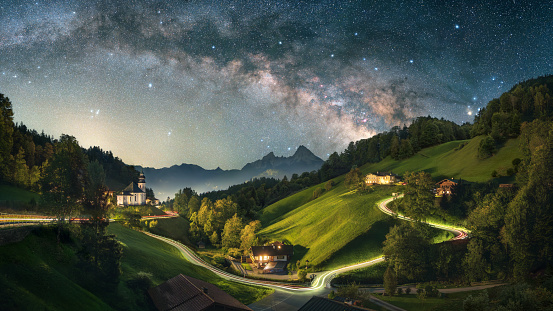 Stunning night shot of iconic landscape in the Alps, an idyllic village with small church and a winding road on the hills lit with car light trails