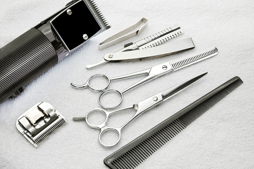 Barber tools including, shears, razor, thinning shears, comb, hair clipper, clipper blade, hair cloth clip, on a terry cloth towel.
