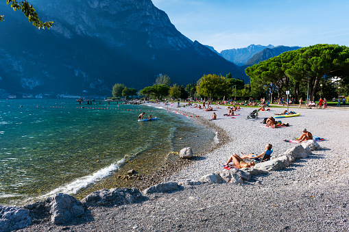 Riva del Garda, Italy - September, 30. 2023:  People lie on the beach at Lake Garda in Riva del Garda.