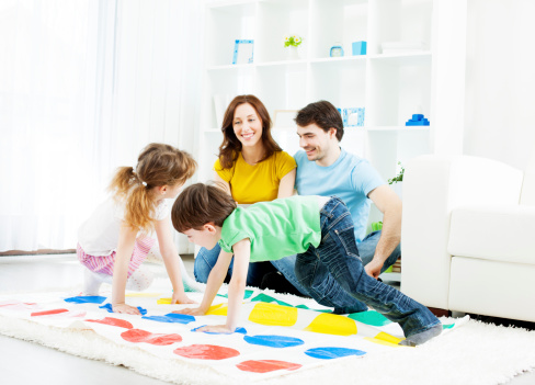 Family with two children playing floor game at home. Mother and father having fun and smiling looking their children.