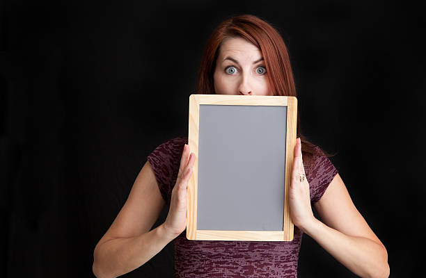 Stressed Woman Holding Blank Chalkboard Over Mouth A stressed out woman holding a blank chalkboard over her mouth. person holding frame over face stock pictures, royalty-free photos & images