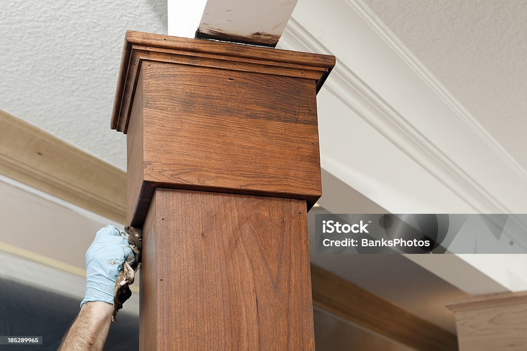 House Painter Applying Stain to a Cherry Column "A house painter, wearing a protective glove, is using a rag to apply stain to a cherry wood column at a high end house construction site." Applying Stock Photo