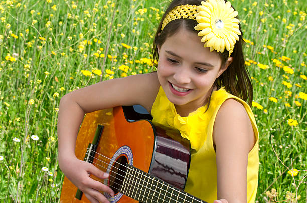 Cute girl playing guitar to daisy field Ten years old girl playing guitar to nature in spring time crown daisy stock pictures, royalty-free photos & images