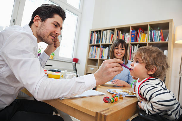 istock Father feeding baby with spoon with mom in background 185290096