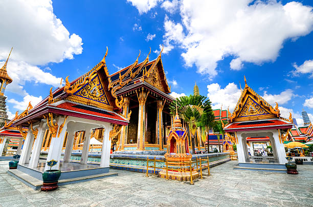 The Emerald Buddha Temple in Grand Palace "Grand Palace and Wat Phra Kaew Temple interior, Bangkok, Thailand. The Emerald Buddha temple. Visible are one of the many Buddha temple in interior of Grand Palace. Dramatic cloudscape with blue sky and cumulus clouds over the Grand Palace. Specific Thai and Buddha Architecture.See more images like this in:" grand palace bangkok stock pictures, royalty-free photos & images