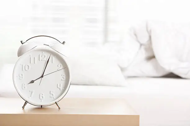 Alarm clock shows eight o'clock, standing on night table at sleeping room.