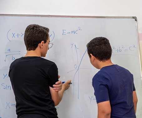 Two students are studying together using the whiteboard in school