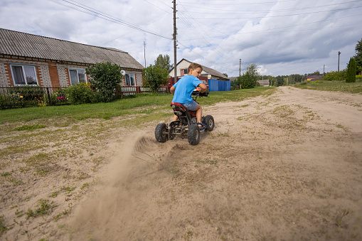 A child rides along a sandy road on an ATV. Quad bike. The wheels of the ATV roll along the dirt road, throwing sand out from under them. A boy is racing on an ATV, turning sharply on a sandy road.