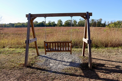 A view behind the wood swinging bench in the park on a sunny day.