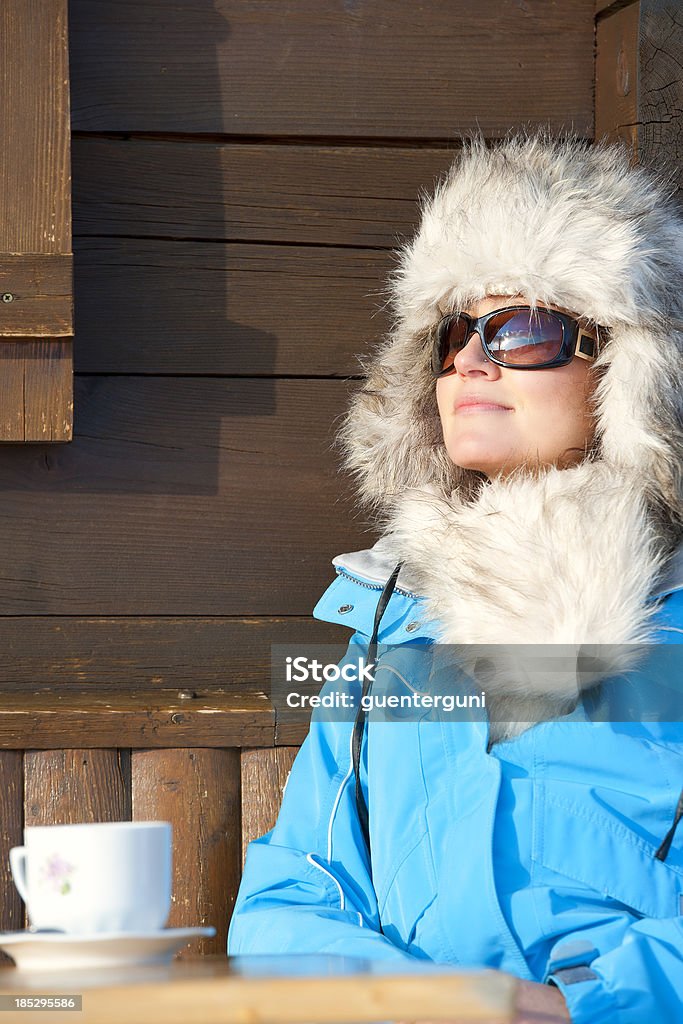 Woman enjoying the sun after skiing Close-up shot of an attractive woman who is enjoying the winter sun at the terrace of a ski chalet. She is dressed up in sportive and fancy outdoor clothes.See related images: Luxury Stock Photo