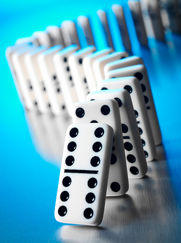 White dominoes with black spots about to achieve the domino effect.Blue lighting on a stainless steel background.Click on the link below to see more of my business images.