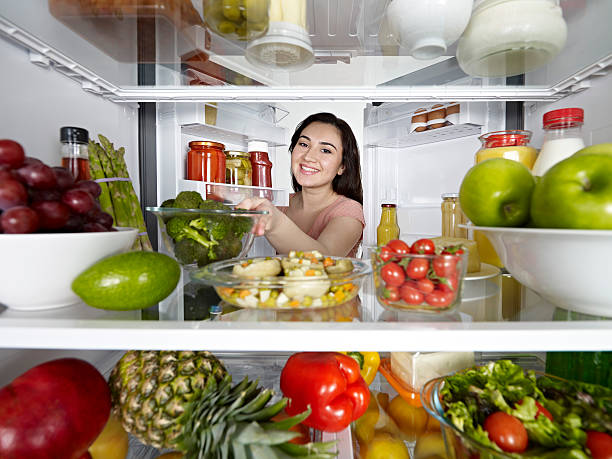 femme prenant brocoli de réfrigérateur - frigo ouvert photos et images de collection