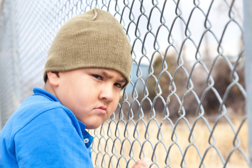 Upset young boy at a fence.