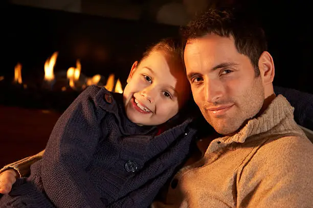 Portrait father and daughter by firelight looking to camera