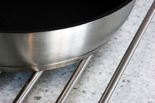 Stainless steel frying pan on a stainless steel trivet resting on a Corian worksurface. The pan is suitable for induction hobs