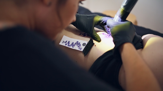 Focused tattooer working machine on client body closeup. Woman drawing outline