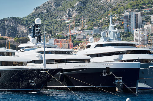 Few huge luxury yachts at the famous motorboat exhibition in the principality of Monaco, Monte Carlo, the most expensive boats for the richest people, mountain and residential complex on background