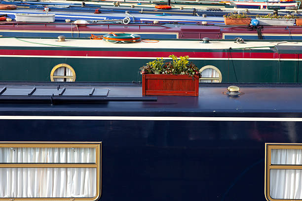 A close-up view of the roofs of several brightly painted narrow boats moored closely together in the Gloucester Docks.  There are window boxes with herbs and greenery on the some of the boats.