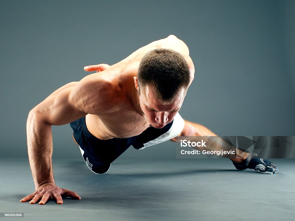 Fitness guy one hand push-up Young handsome guy in black shorts over gray background. He's doing push-ups on one hand One Person Stock Photo