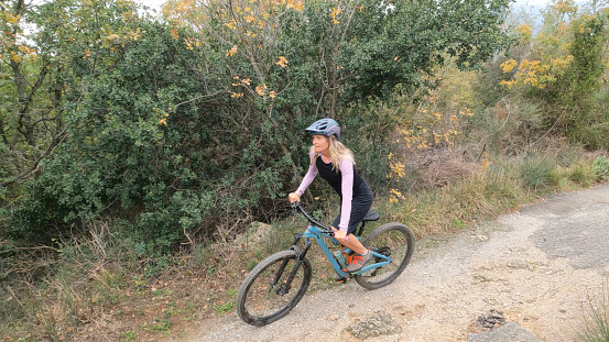 Young woman mountain bikes rural road in forest