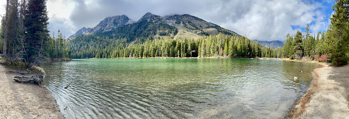 A panoramic image of String Lake shows the turquoise waters in the foreground and the Teton mountains in the background.