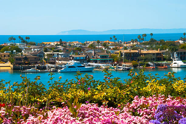 Newport Beach Scene "A scene in Newport Beach in Orange County with houses and yachts in Lido Isle, Newport Bay,  Santa Monica Mountains (and the city of Malibu) in the background and plants and flowers in the foreground." newport beach california stock pictures, royalty-free photos & images