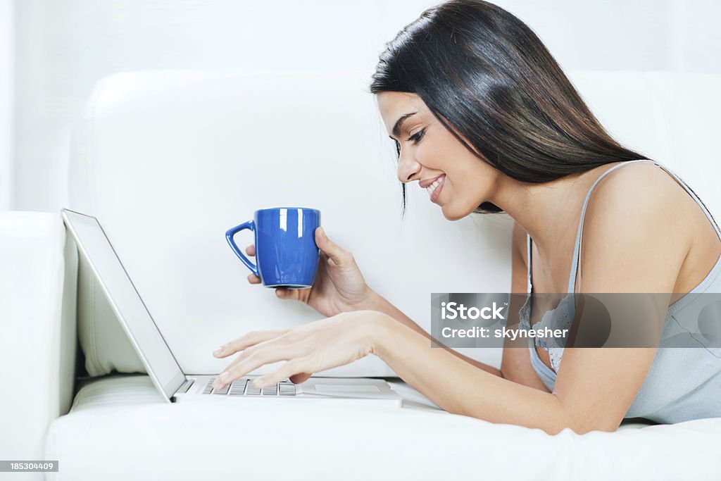 Young woman lying en el sofá con el ordenador portátil. - Foto de stock de Acogedor libre de derechos