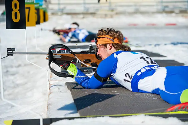 Side view of young male biathlon competitor shooting in lying position