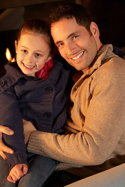 Portrait father and daughter by firelight smiling to camera