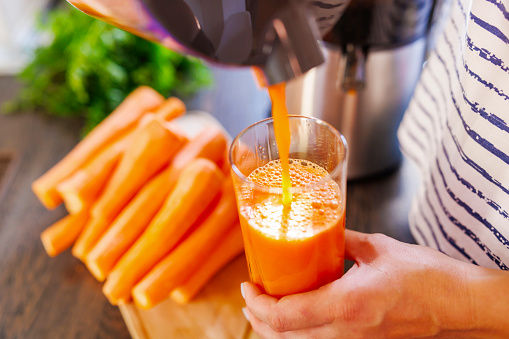 A woman pours fresh carrot juice into glass. Freshly squeezed carrot juice using a juicer