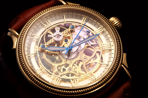 Golden wristwatch with a visible clockwork on black background.