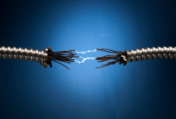 Damaged aluminum conduit with exposed metal wires and charred insulation on blue background. Electicity arcing between the two ends.Other images in this series: