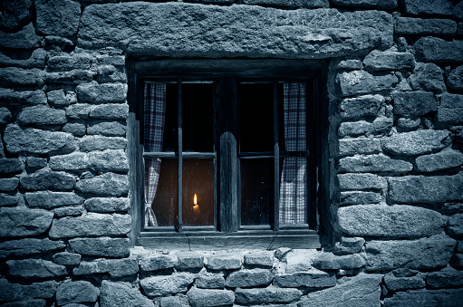 Old window in the moonlight. Inside the house is burning a candle.