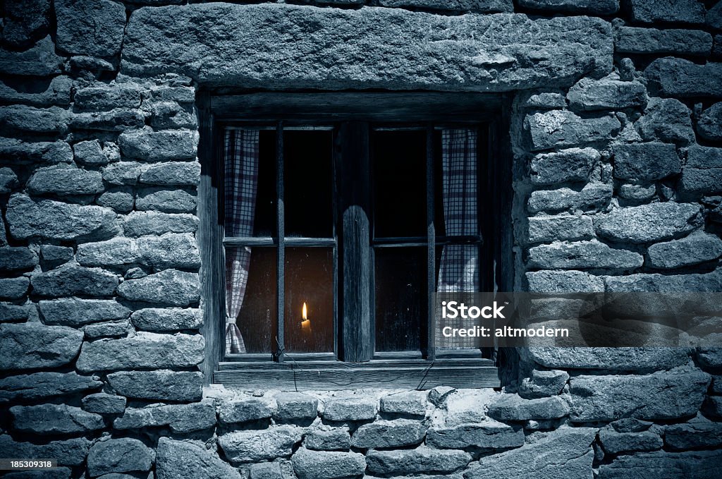 in the night Old window in the moonlight. Inside the house is burning a candle. Window Stock Photo