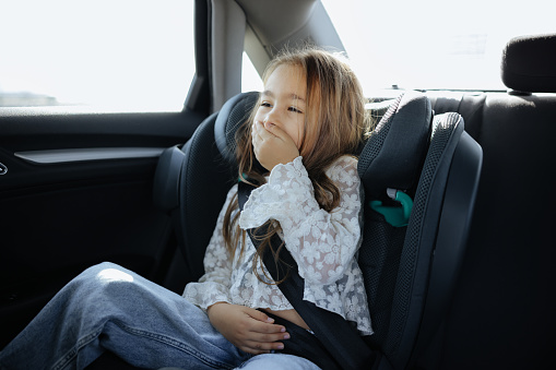 Five years old small child in the backseat of a car sitting in children safety car seat covers his mouth with his hand