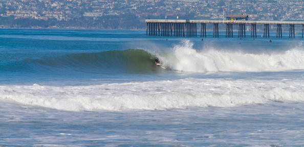 A surfer rides a perfect wave with the San Clemente pier in the background.