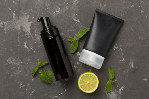 Men cosmetic bottles with mint leaves on concrete background, top view
