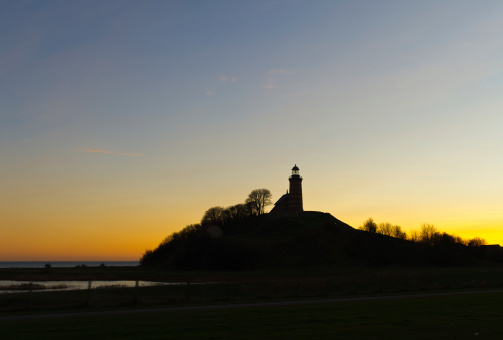 the sun sets behind the lighthouse on the small island near the store belt bridge