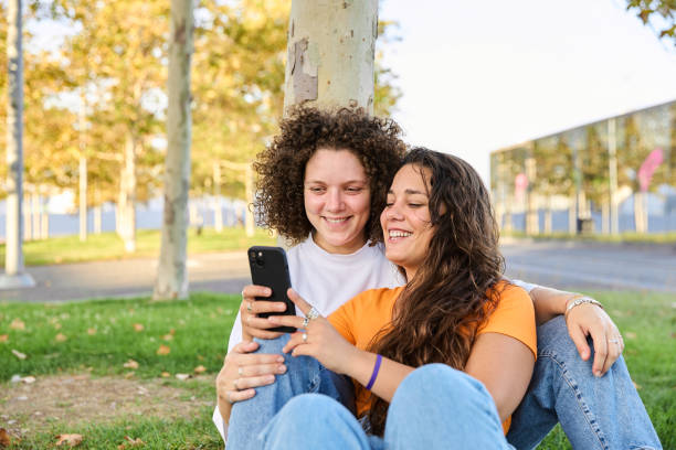 istock Young lesbian couple using mobile phone browsing social networks sitting in a park 1853159933