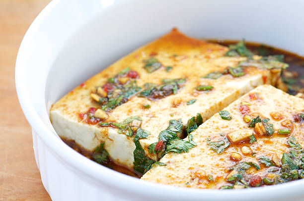 White bowl of slices of tofu in marinade of herbs and spices