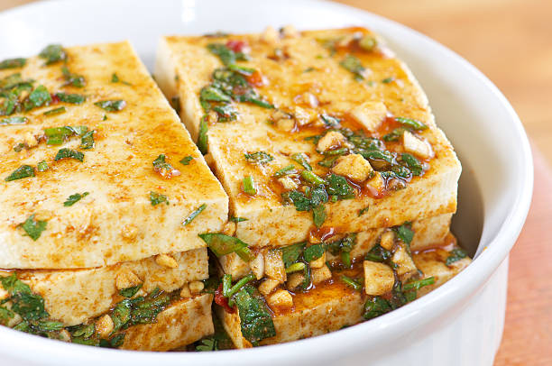 Stack of tofu slices marinating in herbs and spices in white bowl