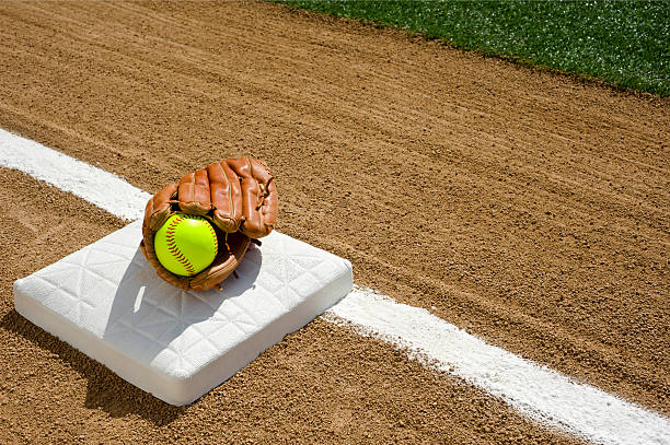 Softball - First base A new fluorescent yellow softball in glove sitting on first base.  baseline stock pictures, royalty-free photos & images