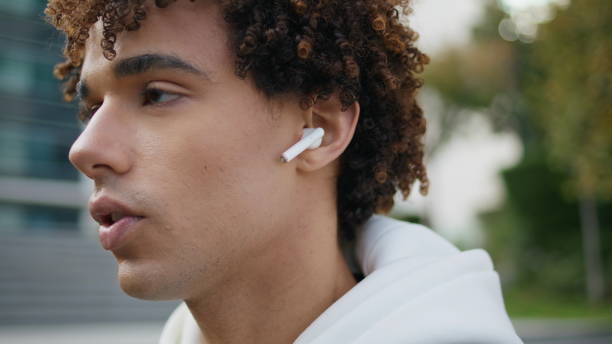 istock Serious model face talking earphones at street portrait. Curly guy using earbuds 1853188409
