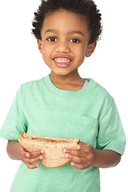 "adorable little boy holding a peanut butter and jelly sandwich, smiling and isolated on white background"