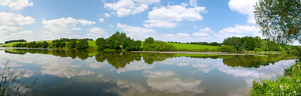 green hills in sunlight. Cloudy sky with mirroring in a lake. Photo taken in Thuringia, Germany