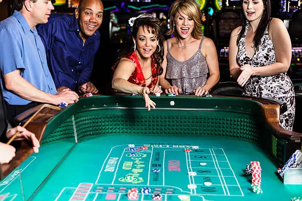 A diverse group of people playing at a craps table inside a casino.