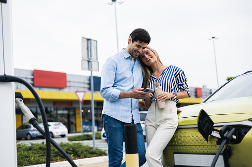 Happy young couple is charging an electric car in the parking lot